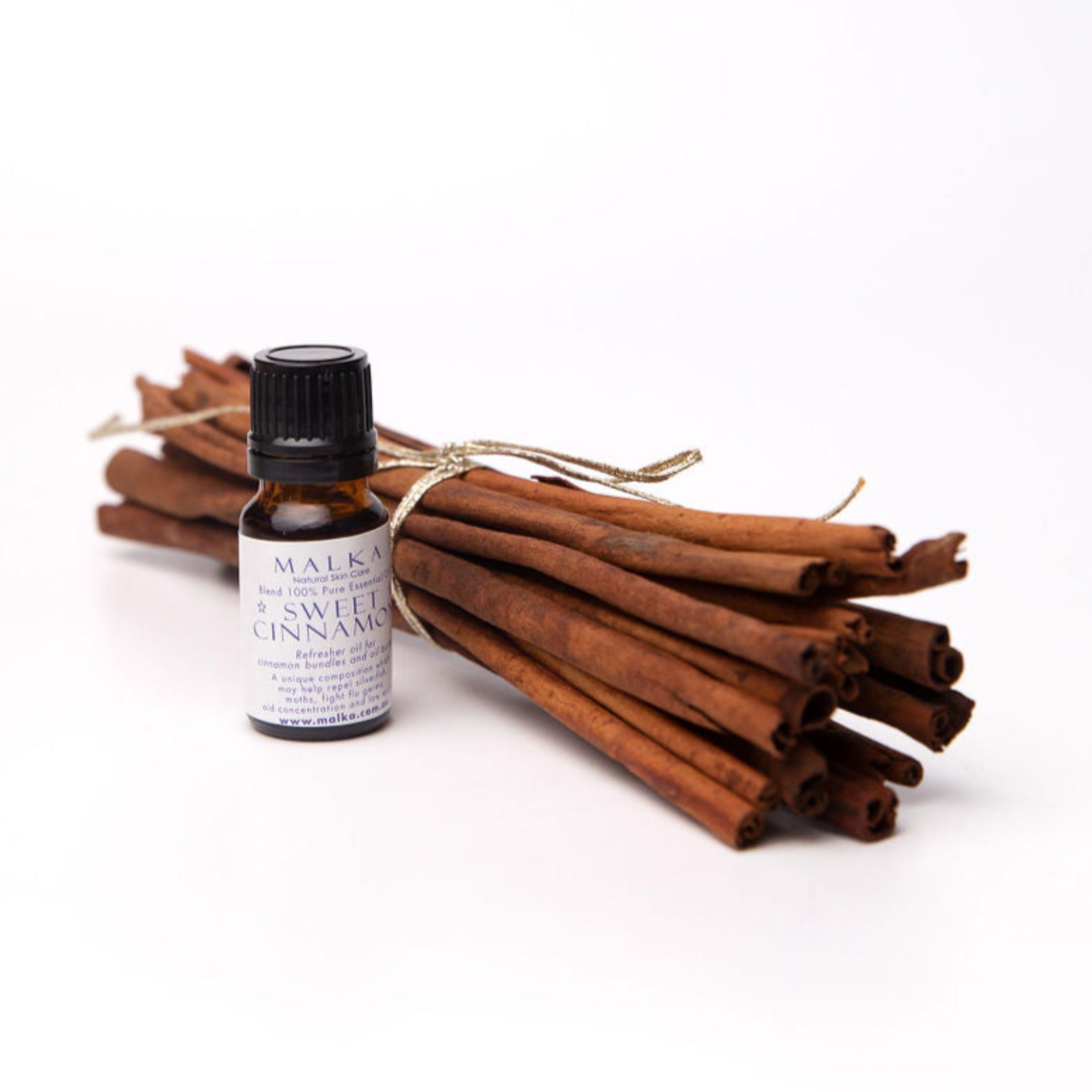 Malka Sweet cinnamon oil sitting beside a bunch of cinnamon quills